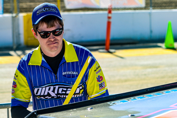 A technical official checks the height of a race car with a tape measure. 